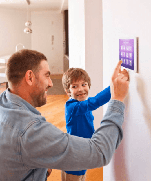 Uśmiechnięty mężczyzna i chłopiec obsługują panel sterujący na ścianie w nowoczesnym, jasnym wnętrzu mieszkania.