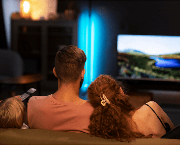 Rodzina siedząca na kanapie, oglądająca telewizję w przytulnie oświetlonym salonie.