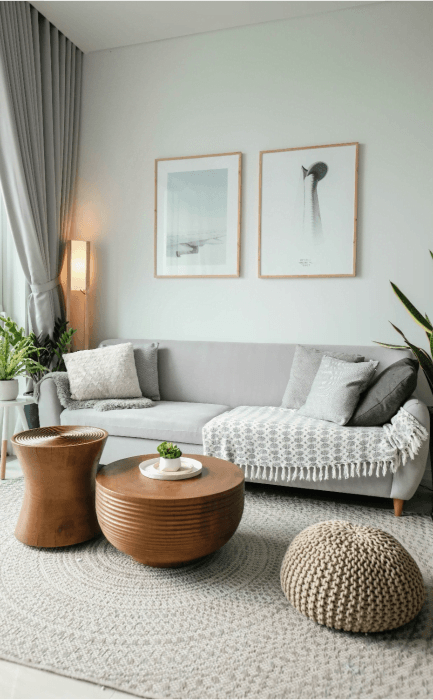 Nowoczesny, jasny salon z szarą sofą, drewnianymi stolikami i ozdobnymi obrazami na ścianie.