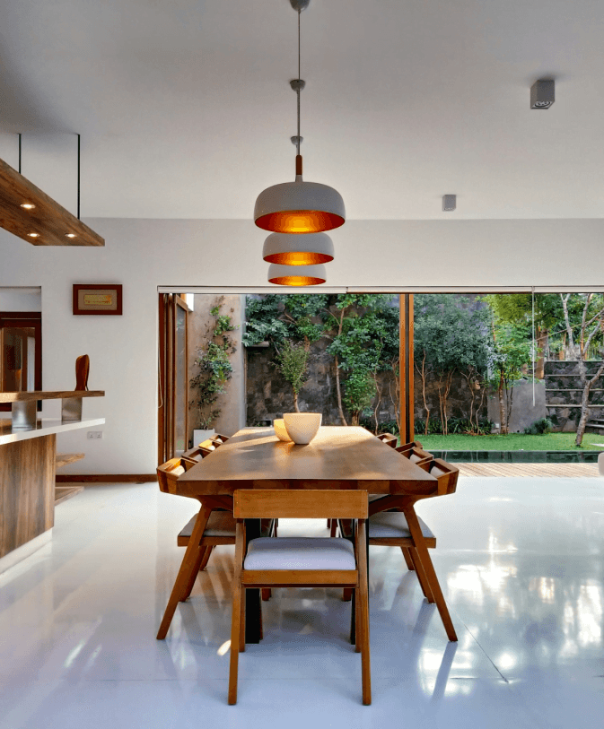 Stylowa jadalnia z drewnianym stołem, designerskimi lampami i widokiem na zielony ogród przez przesuwane drzwi.