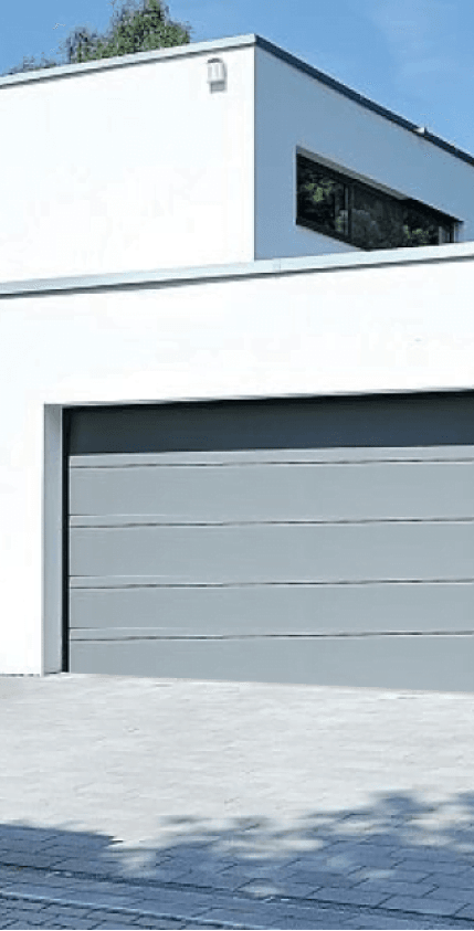Nowoczesny biały budynek z zamkniętą, szeroką bramą garażową w kolorze szarym.