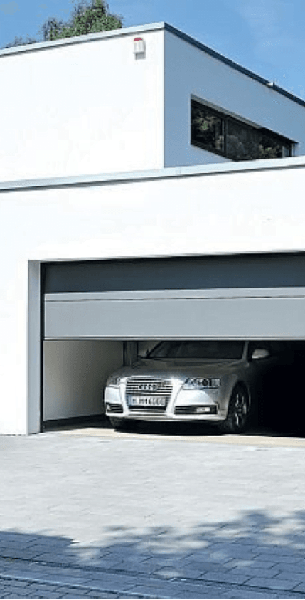 Nowoczesny biały dom z częściowo otwartą bramą garażową, w środku srebrny samochód osobowy.