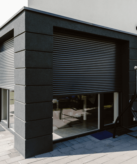 Zbliżenie na grafitowe rolety zewnętrzne zasłaniające duże okna w nowoczesnym budynku.