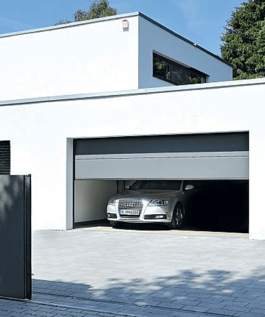 Nowoczesny biały dom z częściowo otwartą bramą garażową, w środku srebrny samochód osobowy.