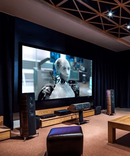 Wnętrze sali kinowej z dużym ekranem, na którym wyświetlany jest robot z filmu science fiction, wokół sprzęt audio i głośniki.