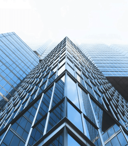 Wysoki szklany wieżowiec ukazany w perspektywie od dołu, odbijający niebo i sąsiednie budynki.