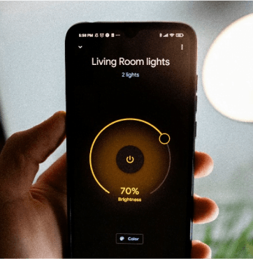 Osoba trzyma smartfon z aplikacją do sterowania oświetleniem w salonie, ustawionym na 70% jasności.