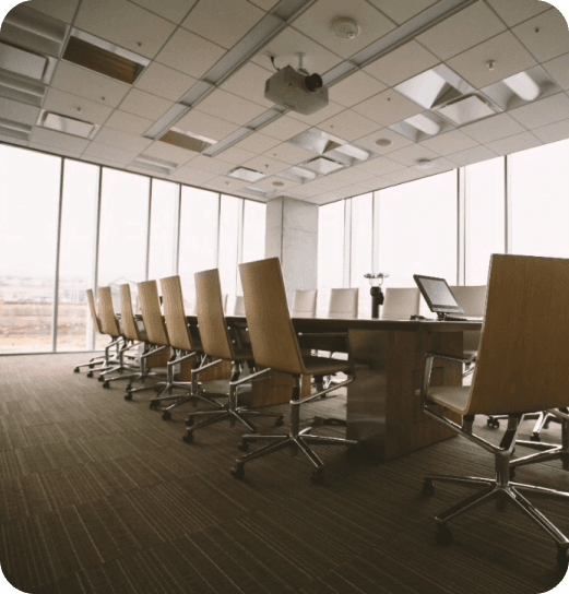 Duża sala konferencyjna z długim stołem, obrotowymi krzesłami i panoramicznymi oknami z widokiem na zewnątrz.