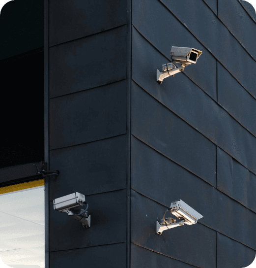 Trzy kamery monitoringu zamontowane na rogu nowoczesnego budynku wykończonego ciemnymi panelami.