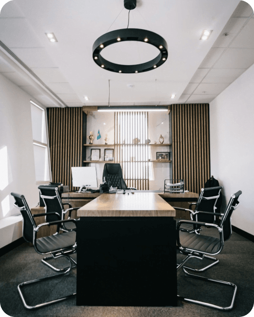 Nowoczesne biuro dyrektora z drewnianym stołem konferencyjnym, czarnymi krzesłami i designerską lampą sufitową.