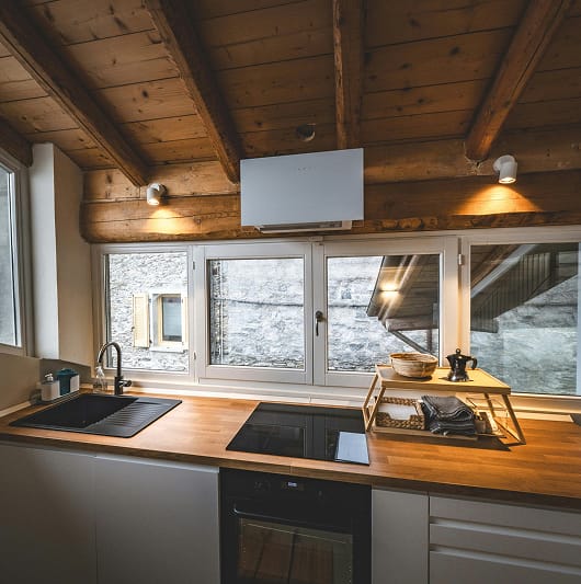 Drewniana kuchnia na poddaszu z dużymi oknami i widokiem na kamienny budynek.